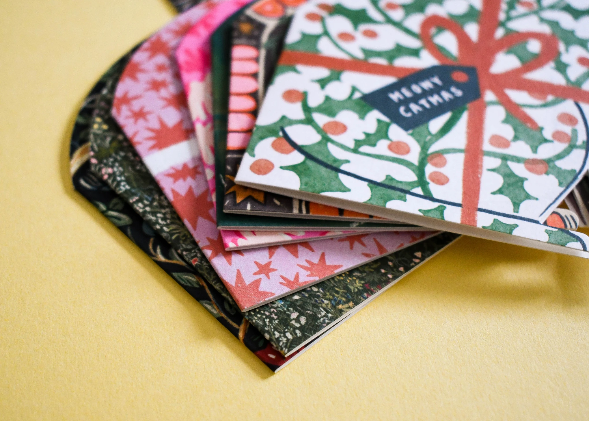Fanned stack of Christmas cards, the top one a holly and ribbon design reading Meowy Catmas.