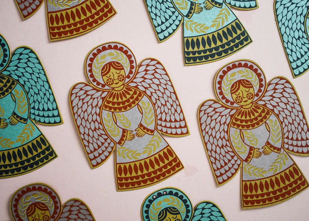 Die-cut angel shapes printed in red, teal, gold and silver, laid out on pink.