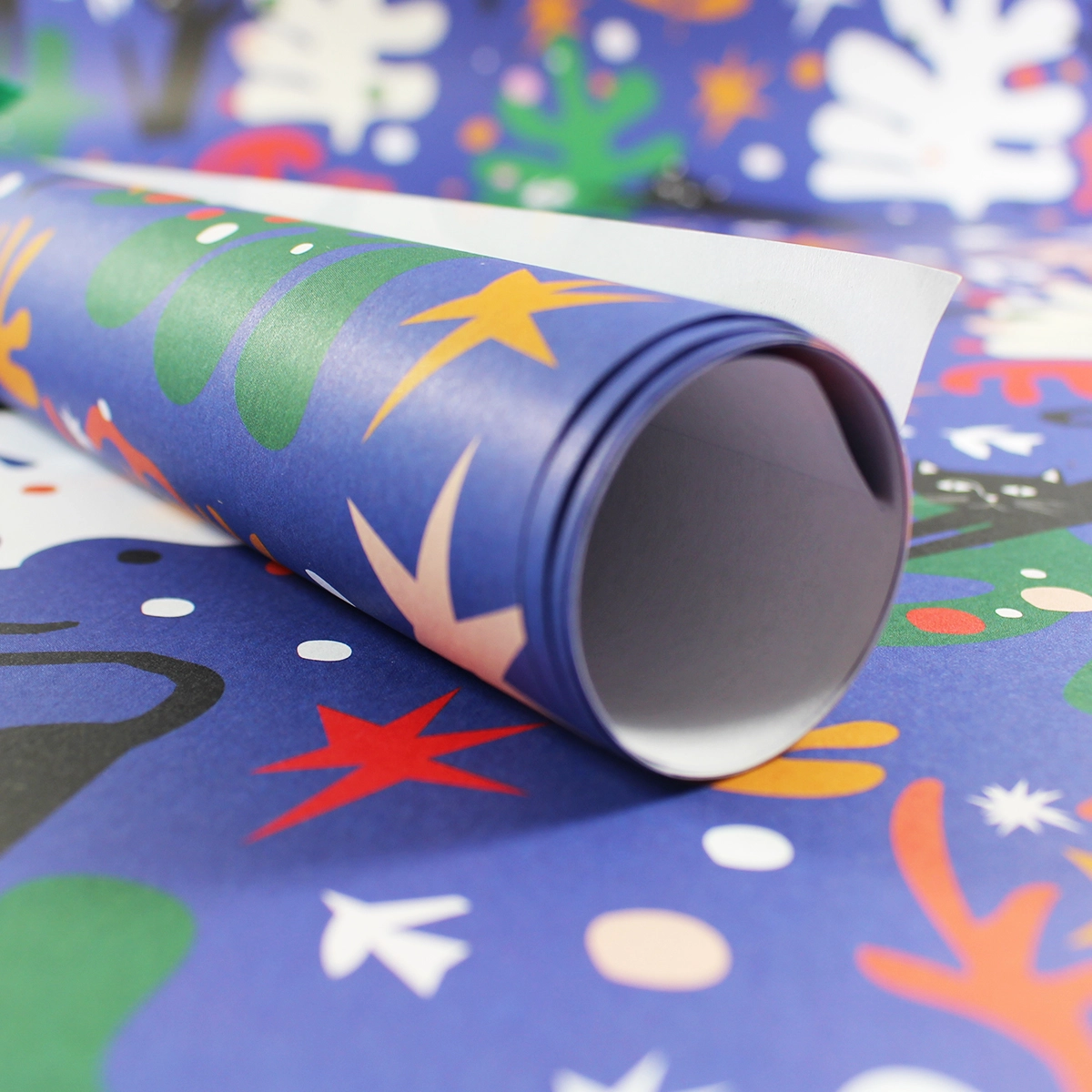 Part-rolled sheet of gift wrap, black cats and cut-out leaf shapes on blue.