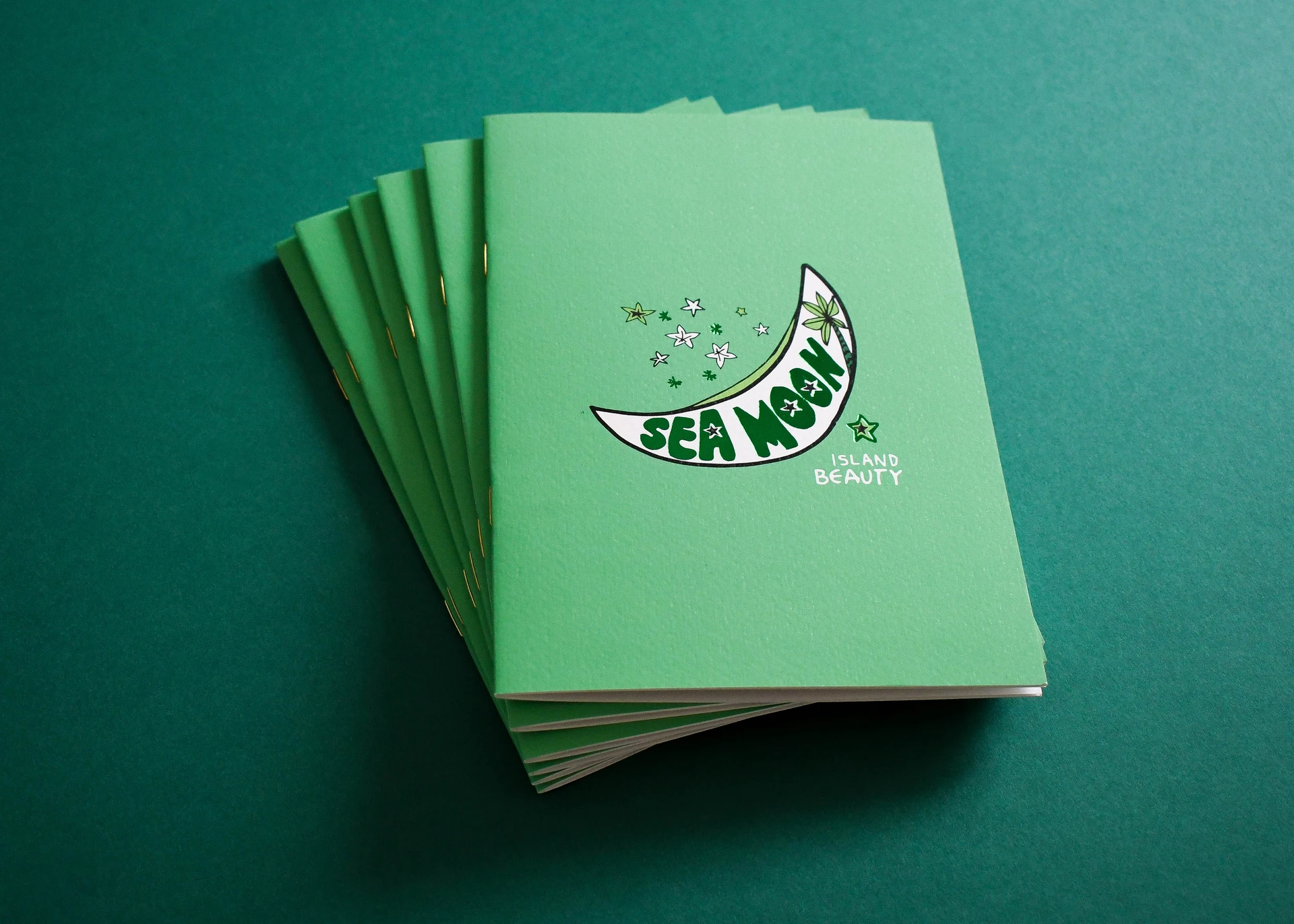A fanned stack of Sea Moon spa menus in green, saddle stitched with gold coloured staples.