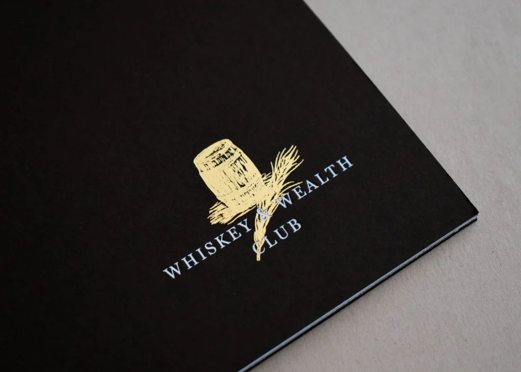 Whiskey & Wealth Club brochure cover, gold foil barrel and barley on black uncoated stock.