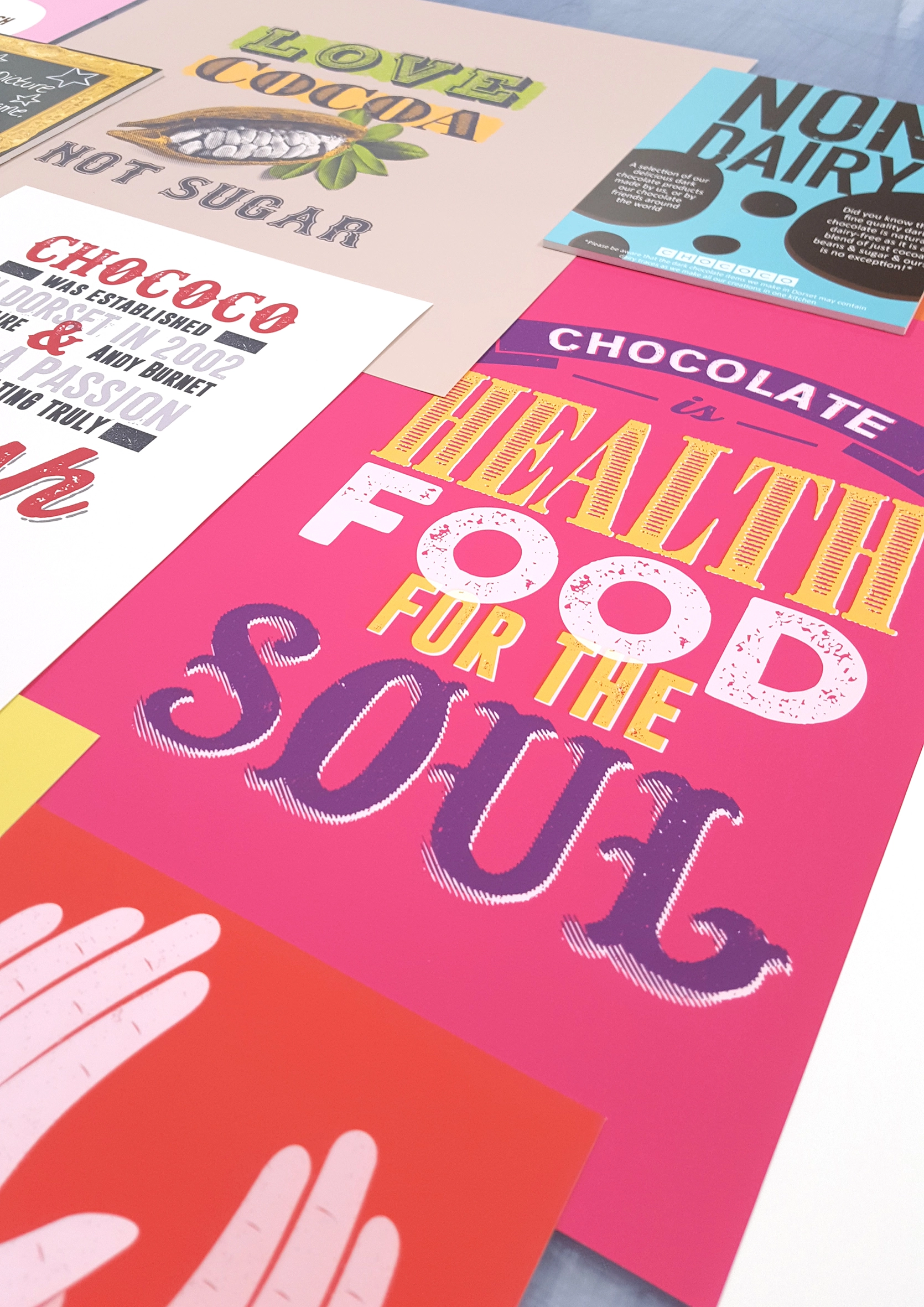 Perspective shot of a vibrant pink poster with bold typography reading 'Chocolate is health food for the soul' surrounded by other prints.