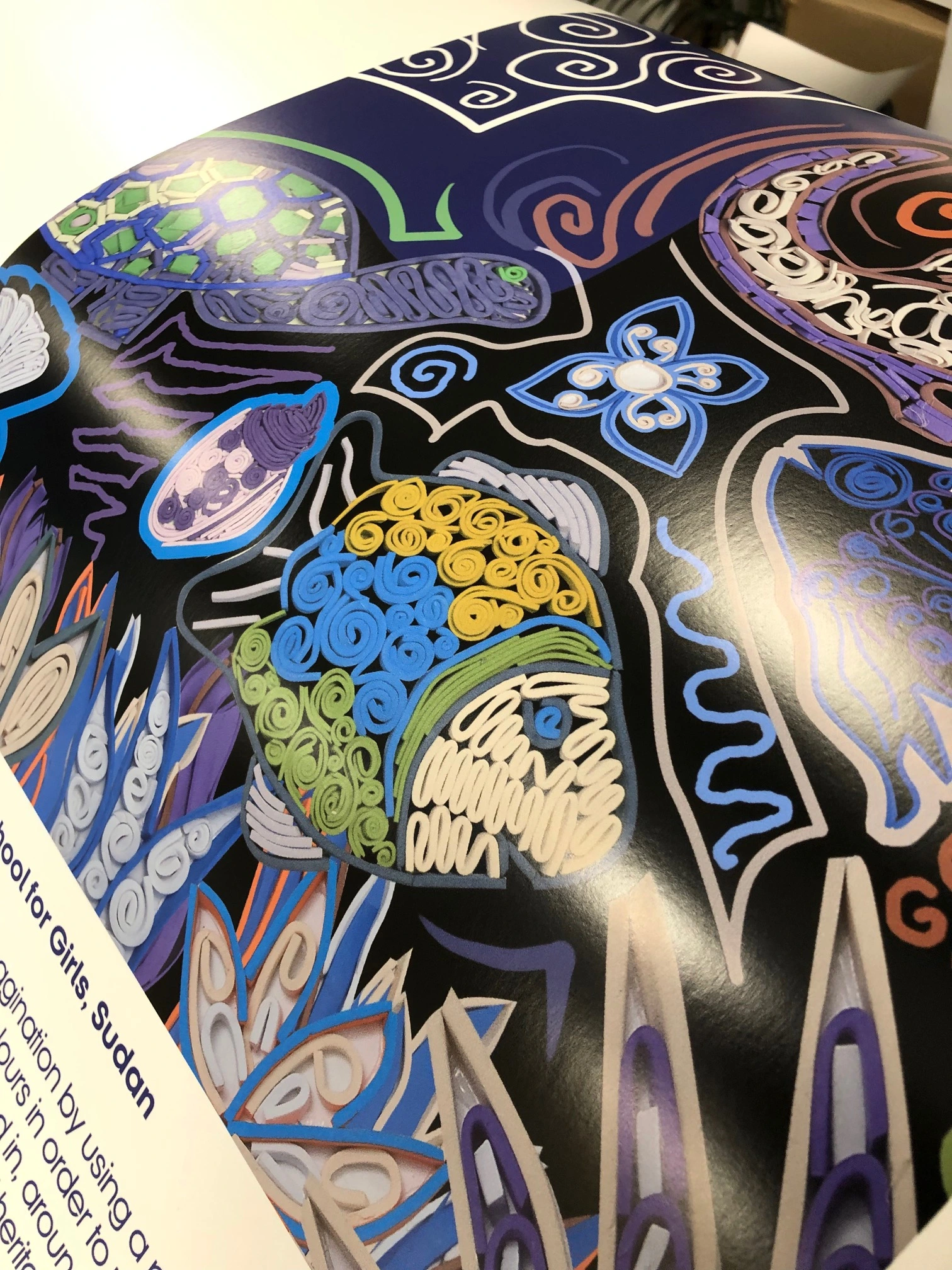 Close-up view of a vibrant art print depicting detailed quilled paper sea creatures, including a colourful fish and sea turtle on a dark blue background.
