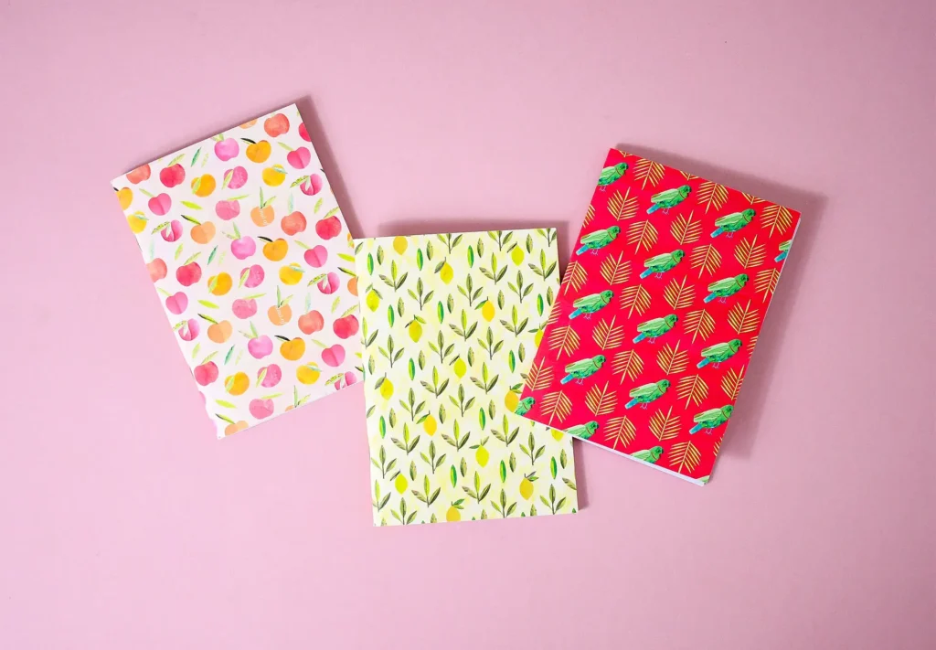 Three notebooks featuring bright illustrations of fruit, plants and birds on the cover.
