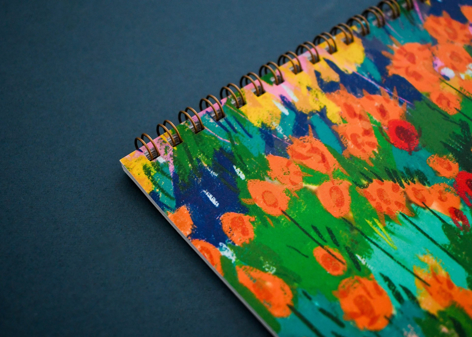 Copper wiro binding along the top edge of a wall calendar with a painted meadow cover.