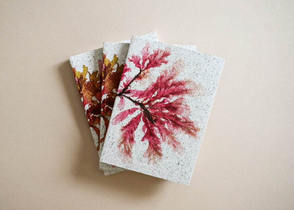 Eco-friendly printed notebooks with autumn leaf cover design, shown stacked on a neutral background