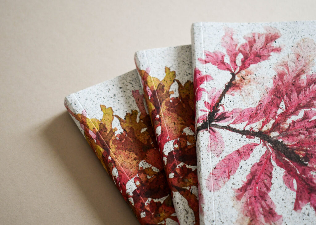 Close-up of sustainable notebook covers featuring hand-painted leaf artwork in red and ochre tones