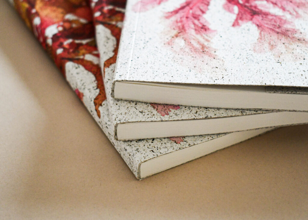 Side view of three printed notebooks showcasing premium binding and textured recycled cover stock