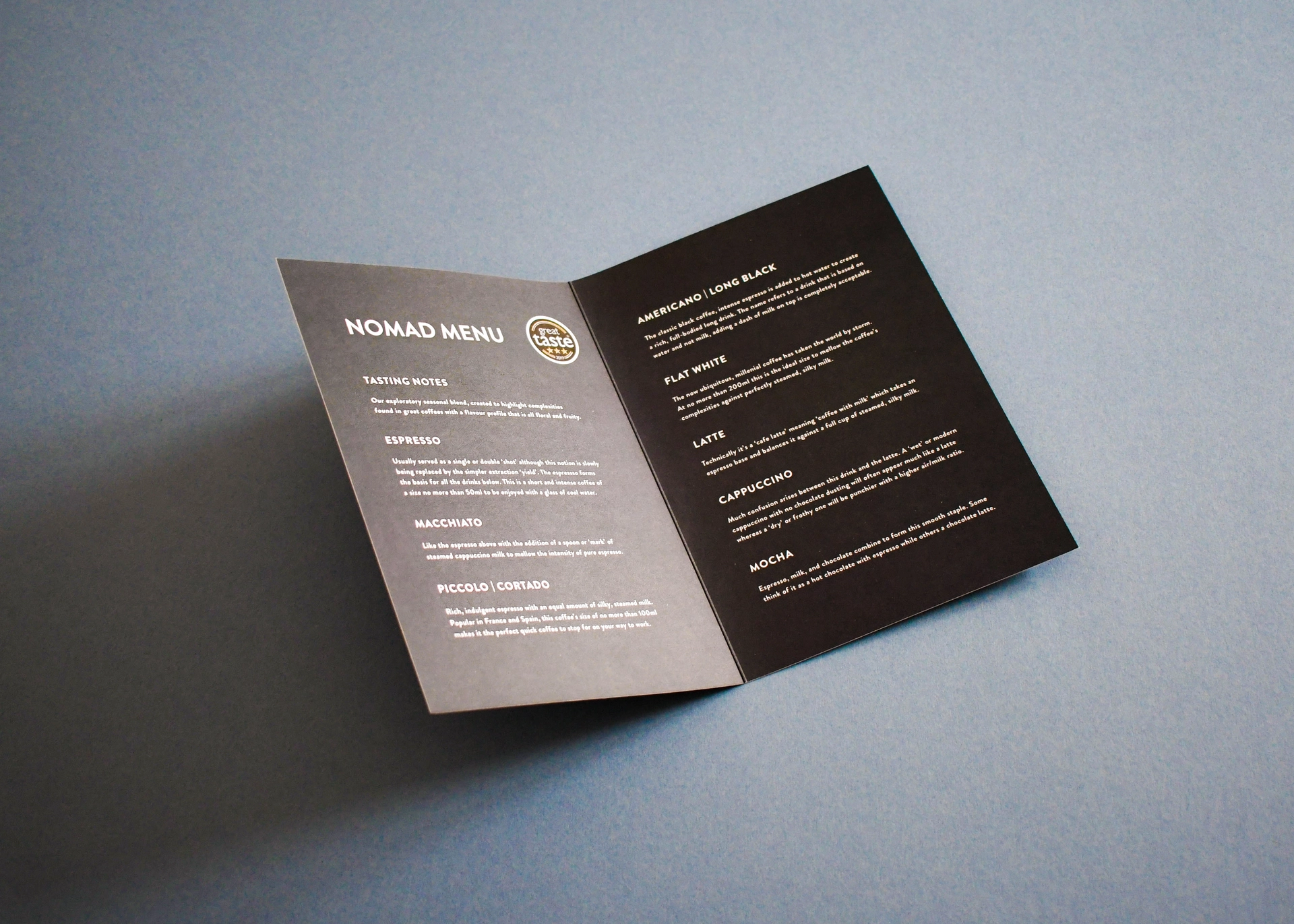 Open folded coffee menu leaflet printed with white text on dark card