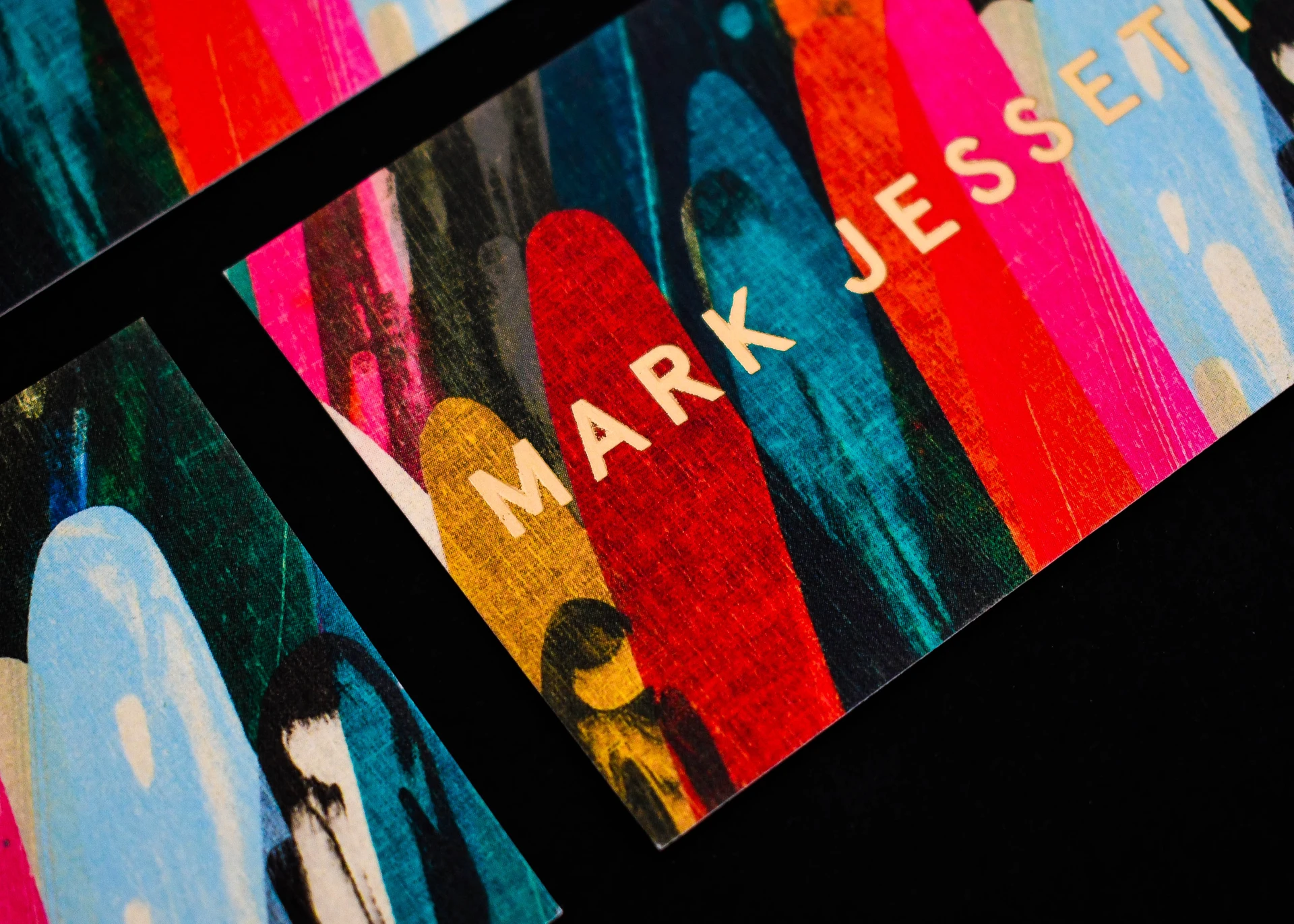 Close-up corner of a colourful business card with "Mark" in gold foil-stamped lettering.