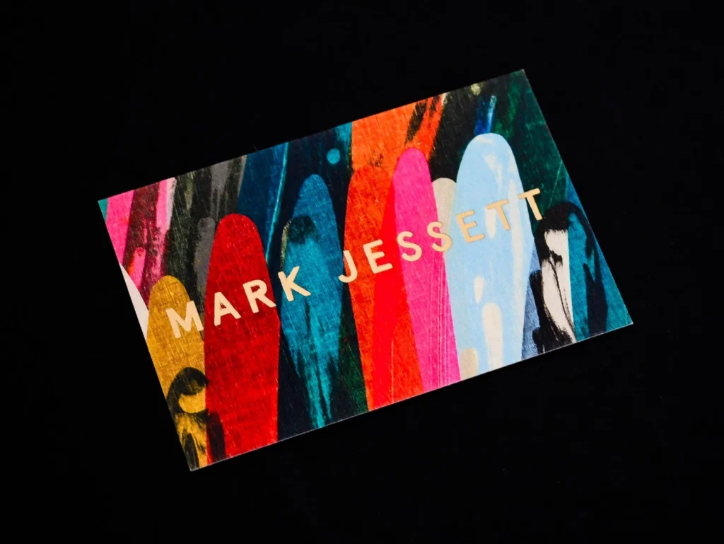 "Mark Jessett" business card on a multicoloured striped background with gold foil-stamped lettering.