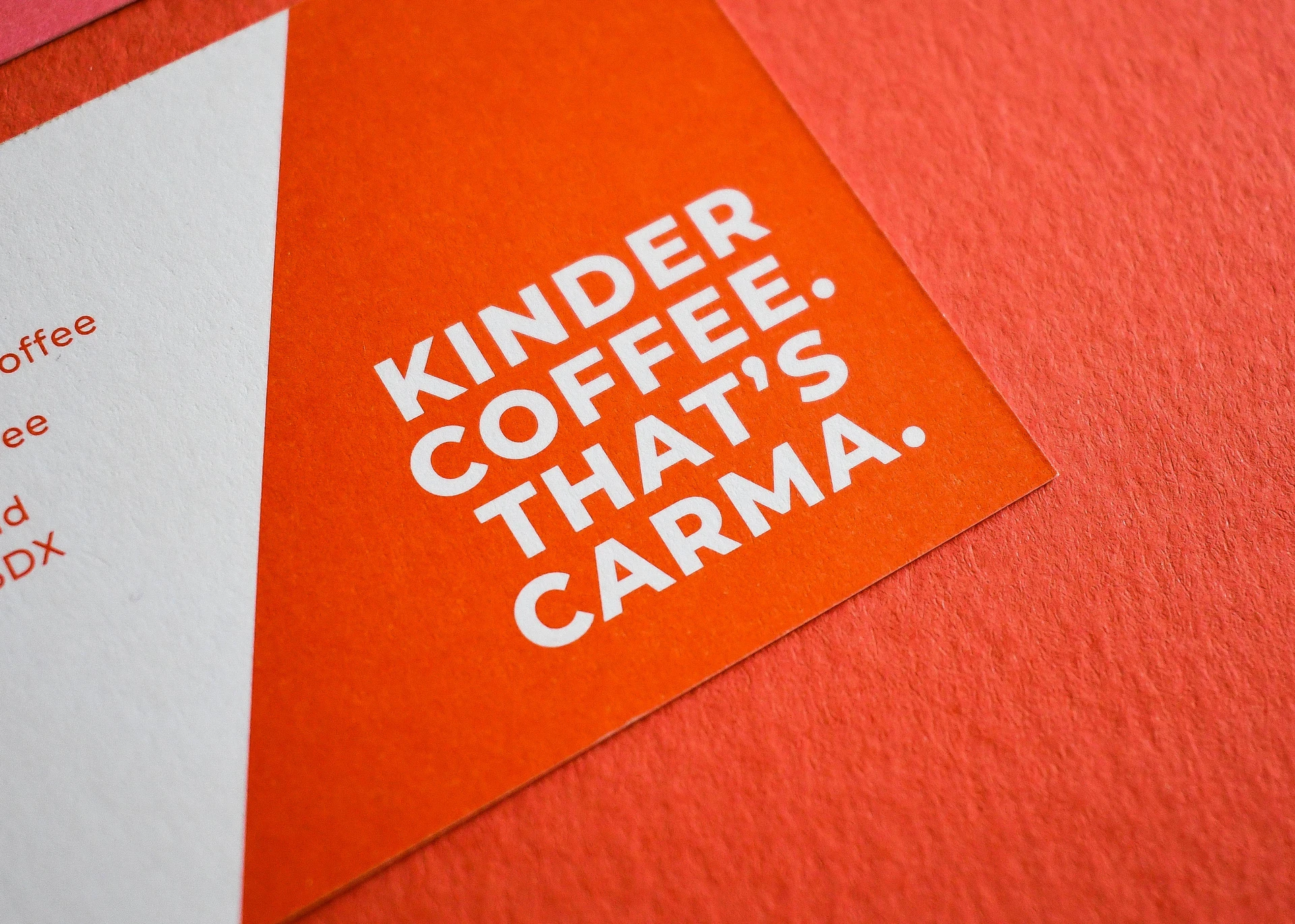 Close-up of an orange "Kinder Coffee" business card with bold white debossed lettering.