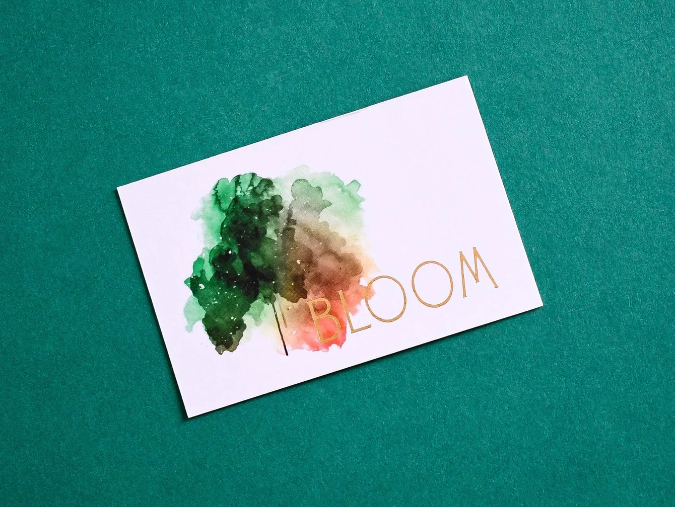 White business card with abstract green and orange watercolor artwork and the word “Bloom” on a green background