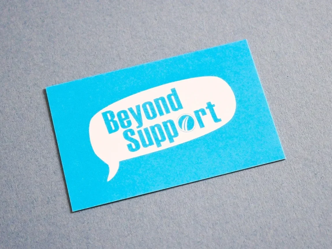 Blue business card featuring a white speech bubble with the text “Beyond Support” on a textured gray background