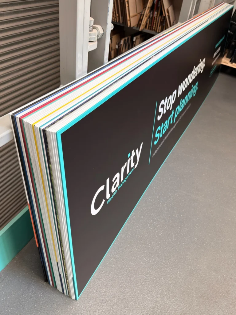 Stack of finished rigid advertising boards leaning in the workshop, printed faces and cut edges visible.