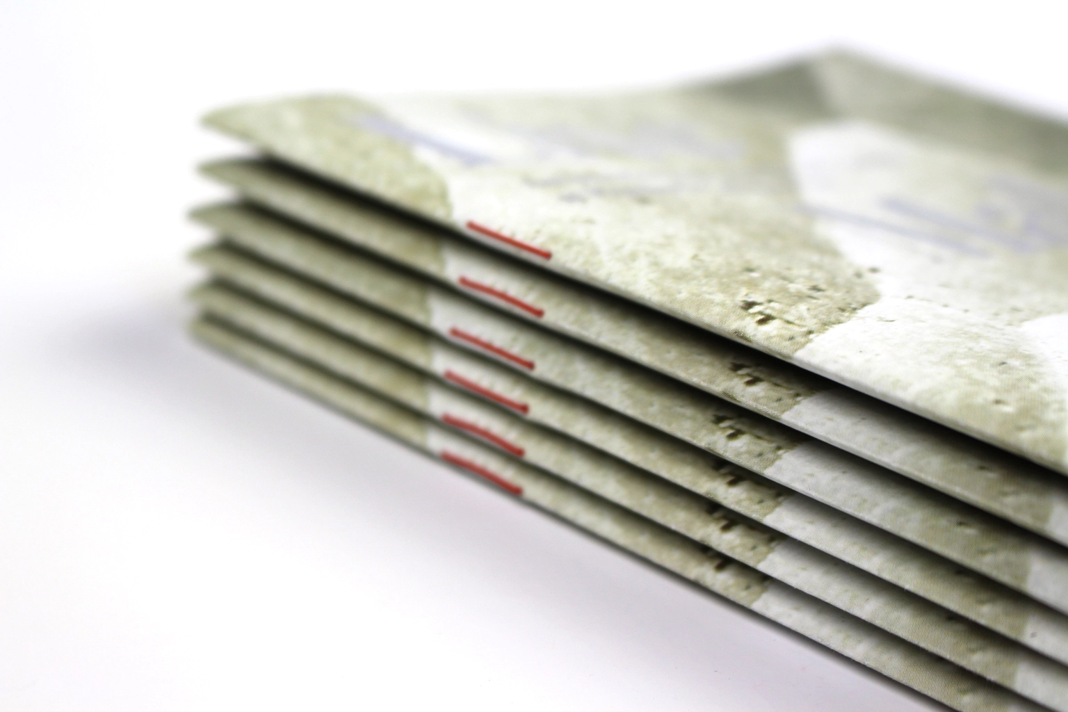 Stack of folded booklets printed on a flecked uncoated stock, red stitching along each spine.
