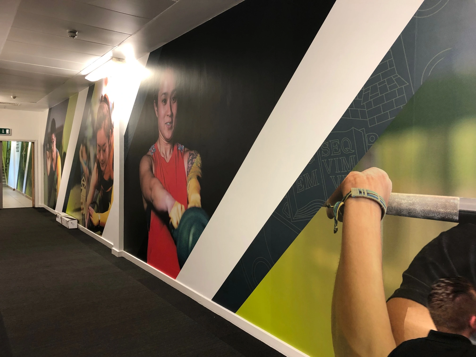 Corridor lined with full-height printed wall graphics of athletes and angled brand colour panels.