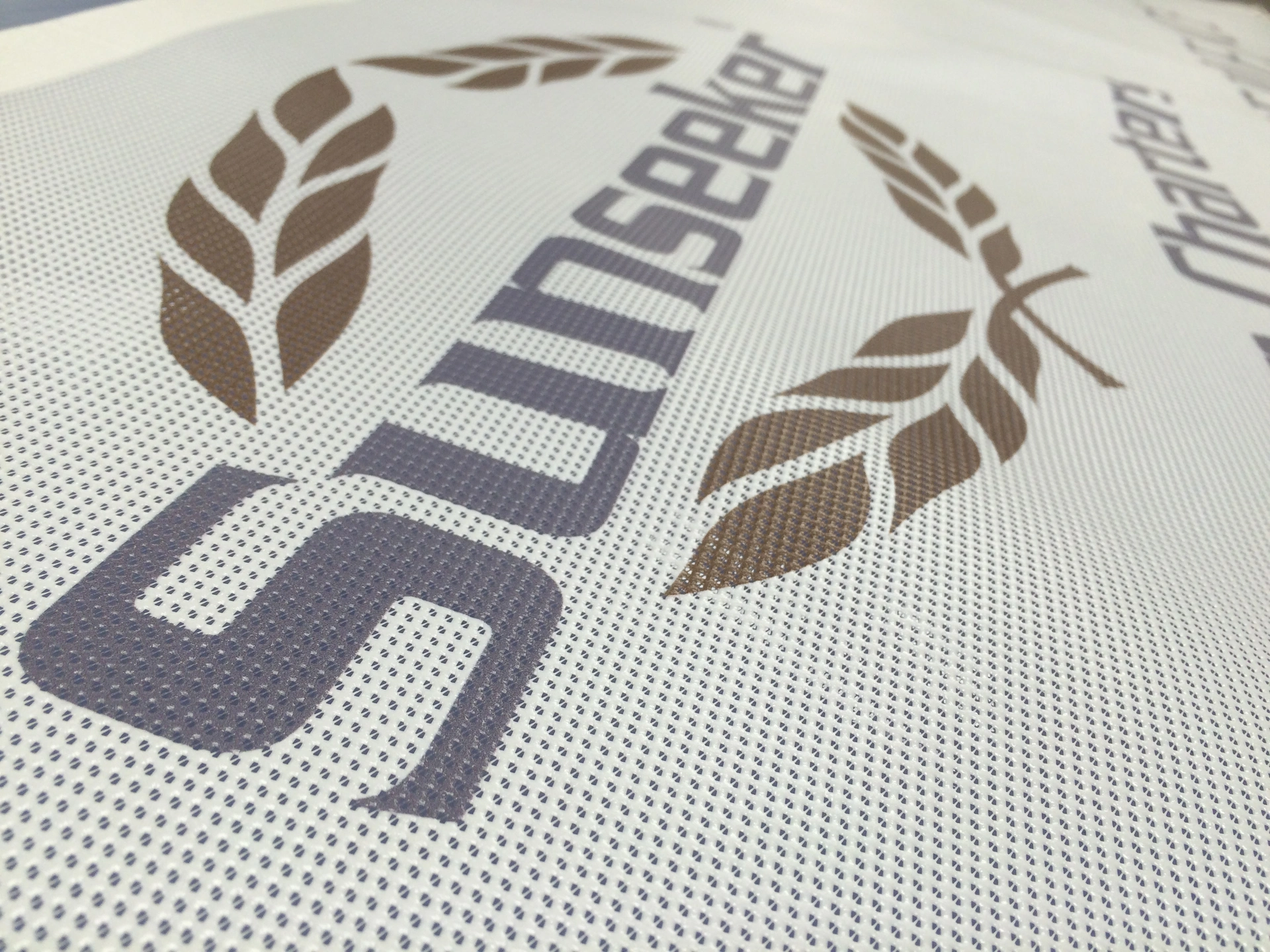 Close-up of a printed mesh banner, showing the perforated weave behind the logo.