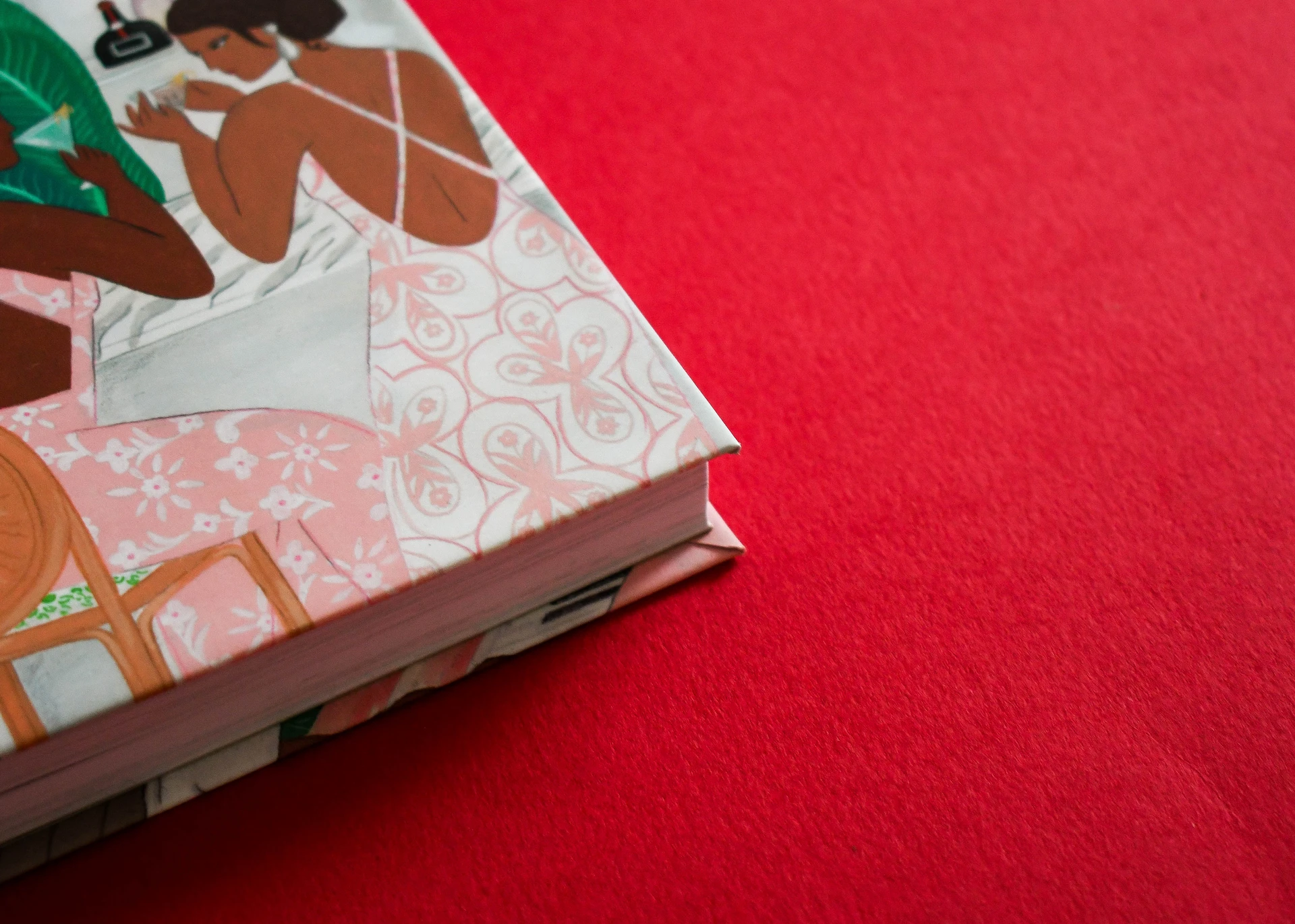 Close-up detail of the corner and block edge of a case-bound hardcover book with an illustrated cover resting on a red surface.