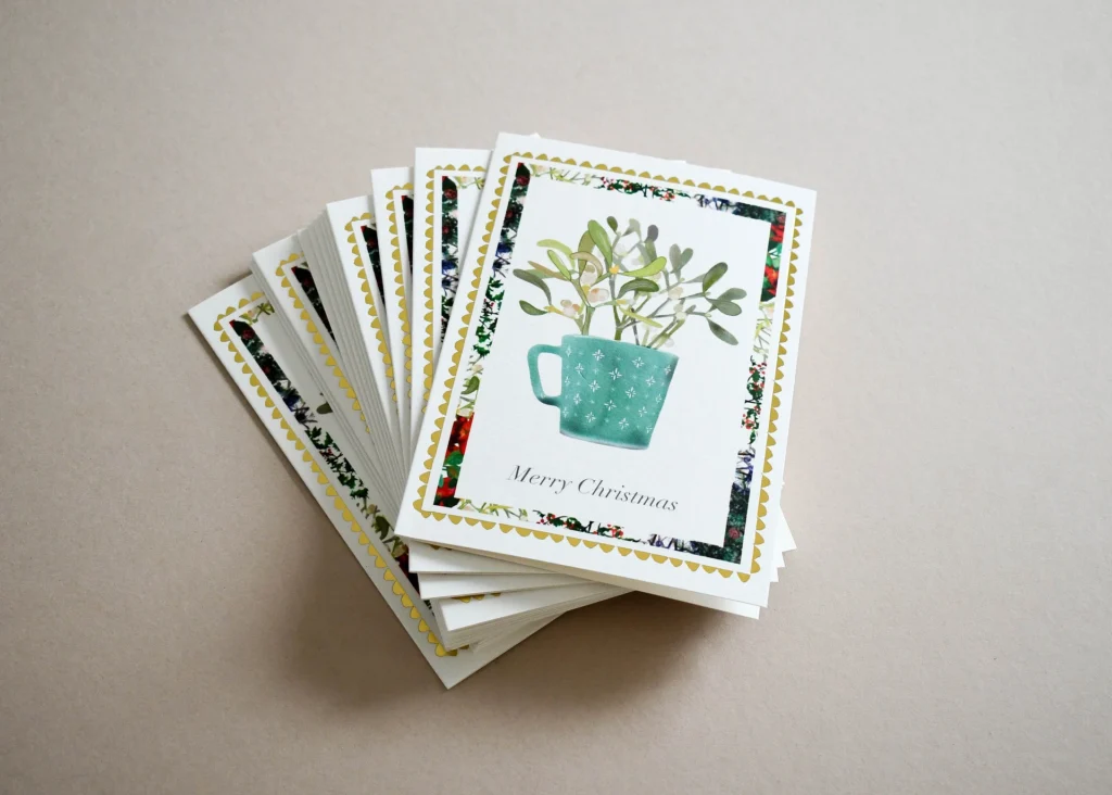 Fanned stack of Christmas cards with a mistletoe design and gold scalloped borders.