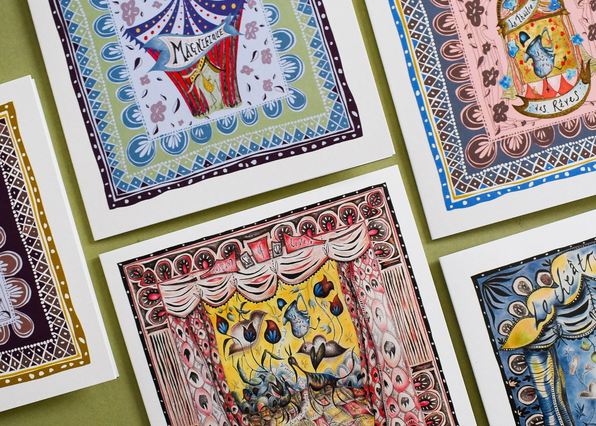 A collection of ornate illustrated greeting cards on a green surface featuring vintage French circus and theater motifs with decorative borders.
