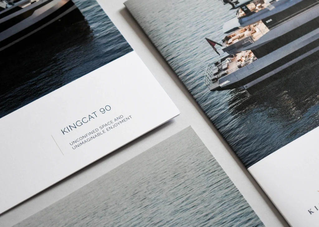 High-angle view of sleek, high-end luxury yacht sales brochures titled KINGCAT 90 laid out on a grey surface.